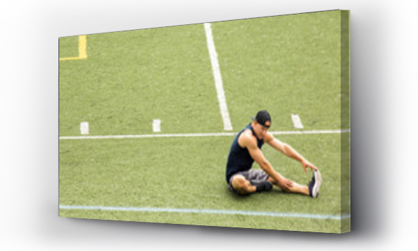 Wizualizacja Obrazu : #146155481 Young man stretching leg while sitting on sports field 