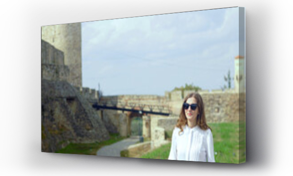 Wizualizacja Obrazu : #1736099237 A smiling millennial woman stands against the backdrop of the medieval architecture of the Belgrade Fortress in Kalemegdan. A female tourist during a must-see sightseeing tour in the capital of Serbia