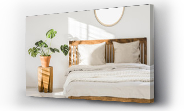 Wizualizacja Obrazu : #211100062 Wooden double bed with white pillows, sheets and knit blanket standing in bright bedroom interior with fresh plant on bedside table and mockup poster on the wall