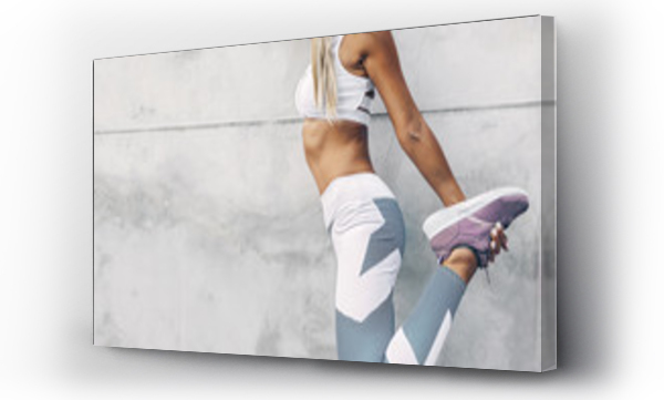 Modelka fitness w stroju sportowym pozująca na tle szarej ściany