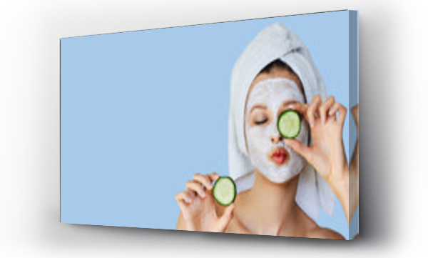 Wizualizacja Obrazu : #265471921 Beautiful young woman with facial mask on her face holding slices of cucumber. Skin care and treatment, spa, natural beauty and cosmetology concept.