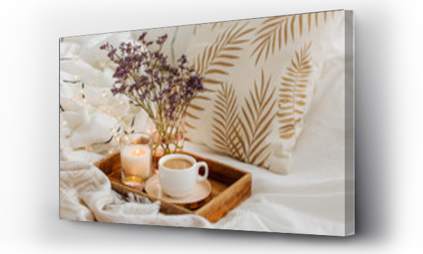 Drewniana taca z kawą i świecami z kwiatami na łóżku. Biała pościel z pasiastym kocem i poduszką. Śniadanie w łóżku. Koncepcja Hygge.