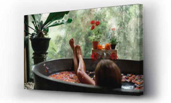 Widok z tyłu kobieta relaksująca się w okrągłej wannie na świeżym powietrzu z tropikalnymi kwiatami, organiczna pielęgnacja skóry, luksusowy hotel spa, lifestyle photo. Kobiece nogi w wannie z płatkami kwiatów