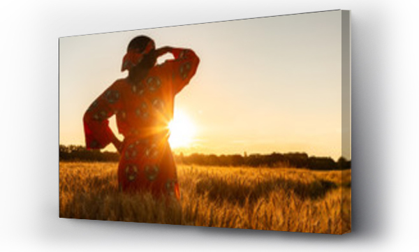 Afrykańska kobieta w tradycyjnym ubraniu stojąca na polu uprawnym o zachodzie lub wschodzie słońca