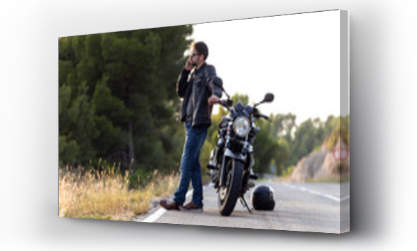 Mężczyzna motocyklista rozmawiający przez telefon z ubezpieczycielem swojego motocykla po tym, jak uległ awarii na drodze.