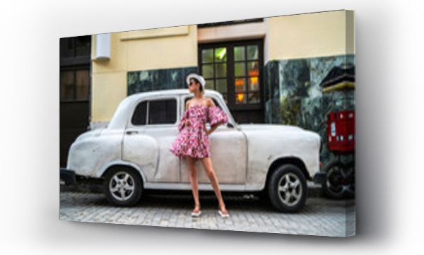 Stylowa kobieta w jasnej sukience i białym kapeluszu obok samochodu retro na ulicy Kuby