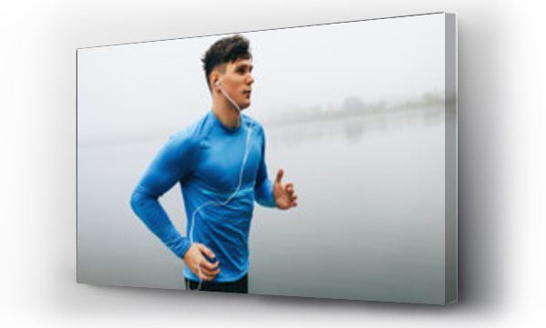 Poziomy odkryty obraz młodego biegacza człowieka biegnącego rano na tle jeziora mgły. Fitness mężczyzna ćwiczący w parku i słuchający muzyki na słuchawkach. Ludzie i sport pojęcie