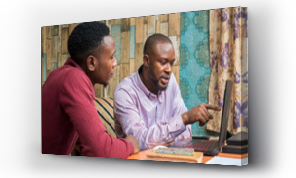 dwóch młodych czarnoskórych ludzi pracujących razem w biurze, patrzących na ekran laptopa, jeden wskazuje coś drugiemu
