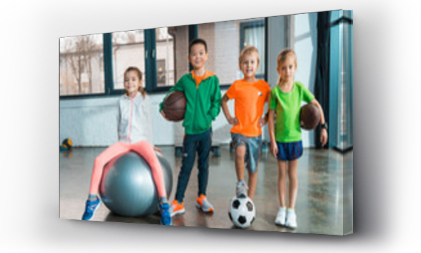 Wizualizacja Obrazu : #324000575 Front view of Child sitting on fitness ball next to multiethnic children with balls in gym