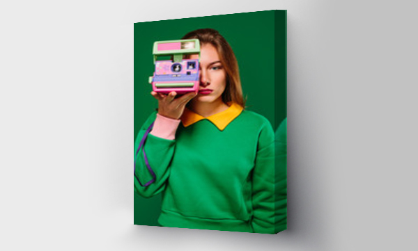 Młoda, bez emocji kobieta w zielonym swetrze, robiąca zdjęcie aparatem retro stojąc na zielonym tle