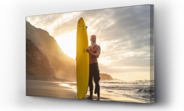 Aktywny senior uprawiający surfing o zachodzie słońca - Sportowy brodaty mężczyzna trenujący z deską surfingową na plaży - Koncepcja aktywnego życia osób starszych i sportów ekstremalnych