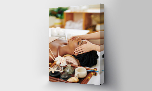 Wizualizacja Obrazu : #371910078 Beautiful young Black woman enjoying face and head massage in spa salon when lying on bed next to tray with aroma oils