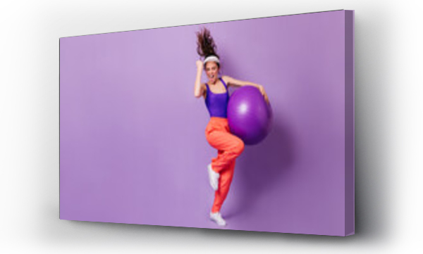 Wizualizacja Obrazu : #409558797 Woman in sports cap and bright top rejoices victory. Portrait of girl in red pants with fitball on purple background