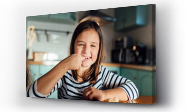 Wizualizacja Obrazu : #431960869 Smiling girl eating tangerine while sitting at dining table in kitchen