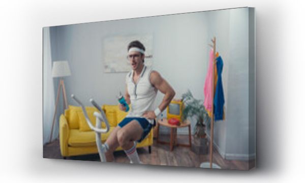 Wizualizacja Obrazu : #457103009 sportsman training on exercise bike and holding sports bottle in living room, retro sport concept