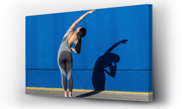 Wizualizacja Obrazu : #462724564 Woman in sports clothing doing exercise in front of blue wall