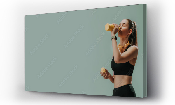 Wizualizacja Obrazu : #507785886 Young sporty woman in sportswear with wireless headset drinking from bottle over green background, copy space