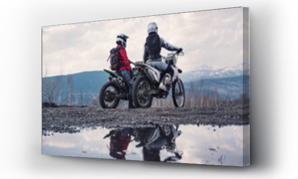 Wizualizacja Obrazu : #508364458 Females wearing helmets and motorcycle gear sitting on dirt motorcycles. Reflection in puddles, snowy peaks on horizon. Offroad travel