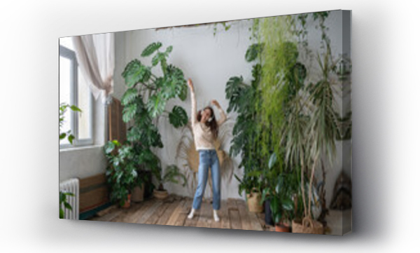 Wizualizacja Obrazu : #513539838 Positive young italian woman in wireless headphones listening to music with pleasure, enjoying the moment, relaxing, dancing on wooden floor in cozy home garden with monstera and tropical plants. 