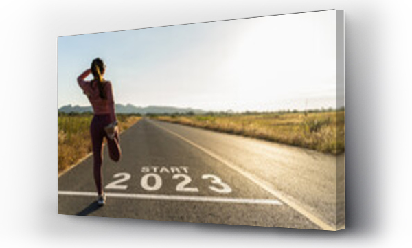 Wizualizacja Obrazu : #553096490 New year 2023 or start straight concept.word 2023 written on the asphalt road and athlete woman runner stretching leg preparing for new year at sunset.Concept of challenge or career path and change.