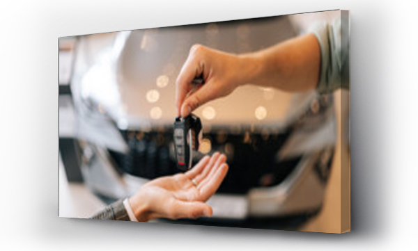 Wizualizacja Obrazu : #644212192 Close-up hands of unrecognizable dealer male giving new car key to customer man in business suit on blurred background of new auto in dealership office. Concept of choosing and buying car at showroom.