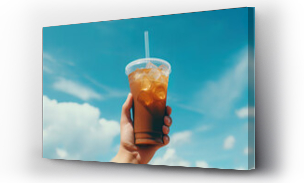 Wizualizacja Obrazu : #655066420 Hand holding iced coffee in a plastic cup with a blue sky and cloud background