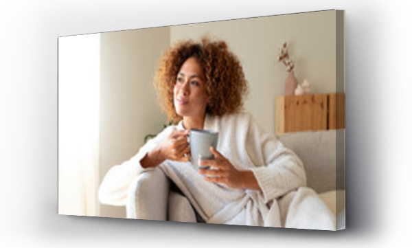Wizualizacja Obrazu : #665912399 Pensive multiracial woman relaxing at home, sitting on the sofa drinking tea.