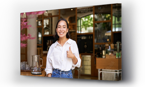 Wizualizacja Obrazu : #668502875 Confident asian businesswoman, showing thumbs up, standing near entrance of her cafe or restaurant, recommending place