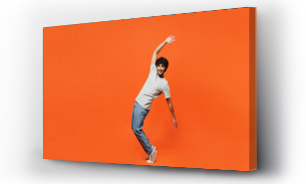 Wizualizacja Obrazu : #671733684 Full body side view young smiling happy Indian man he wears t-shirt casual clothes stand on toes leaning back with outstretched hands isolated on orange red color background studio. Lifestyle concept.