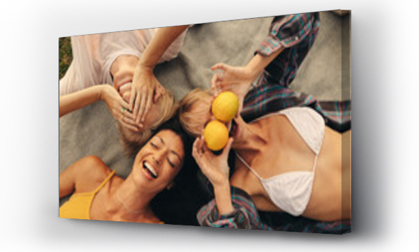 Wizualizacja Obrazu : #690148345 Girlfriends enjoying summer day outdoors, lying down in the park, holding fruits and smiling