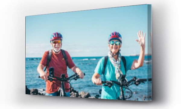 Wizualizacja Obrazu : #691487772 Cheerful senior couple enjoying riding bikes together at sea to be fit and healthy. Active seniors wearing helmets having fun training in outdoors. Authentic elderly retired life concept