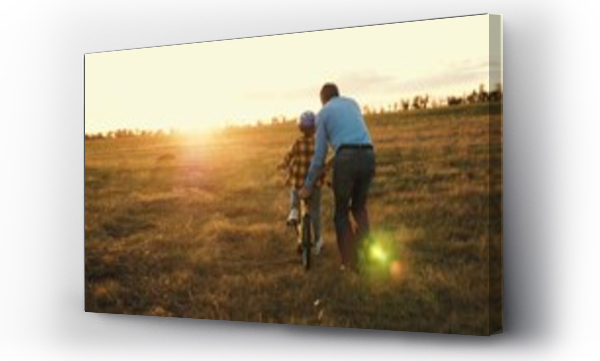 Wizualizacja Obrazu : #693810237 Affectionate papa actively involved in assisting little kid on riding bicycle. Caring dad prevents mishaps holding bike of son. Father provides risk-free bike ride for beloved child in field