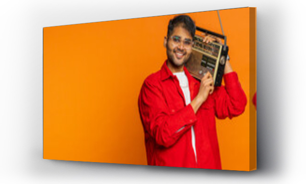 Wizualizacja Obrazu : #697259969 Happy young Indian man using retro tape record player to listen music, disco dancing favorite track, having fun entertaining, fan of vintage technologies. Arabian guy on orange background. Copy-space