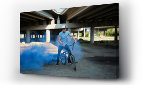 Wizualizacja Obrazu : #699059670 Man with BMX bike emitting blue smoke near bridge