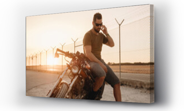 Wizualizacja Obrazu : #771029383 A man talks on the phone sitting on his motorcycle on a road